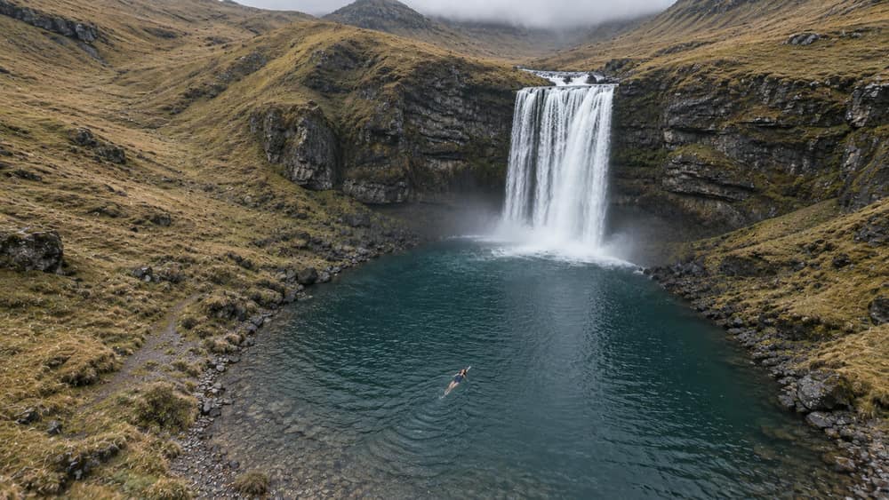 Panel 12, Returning to scale: Aerial wide view of the waterfall and pool, with Nisha reduced to a small figure in the water.