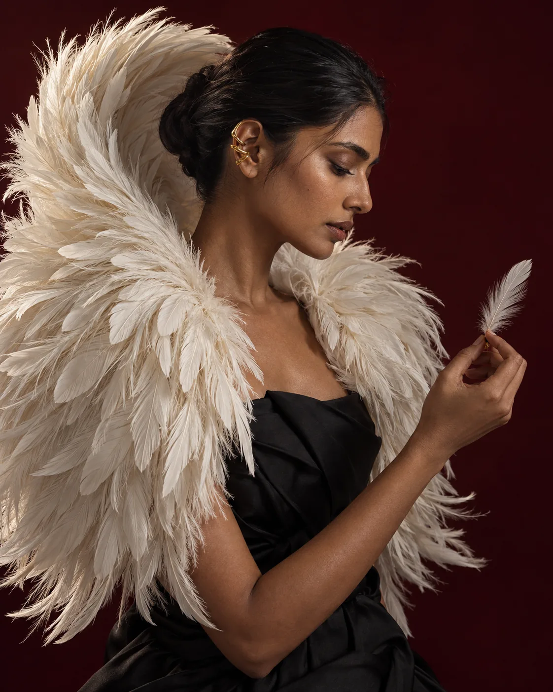 A woman wrapped in a sculpted cape of white feathers holds a single feather against a deep red backdrop.