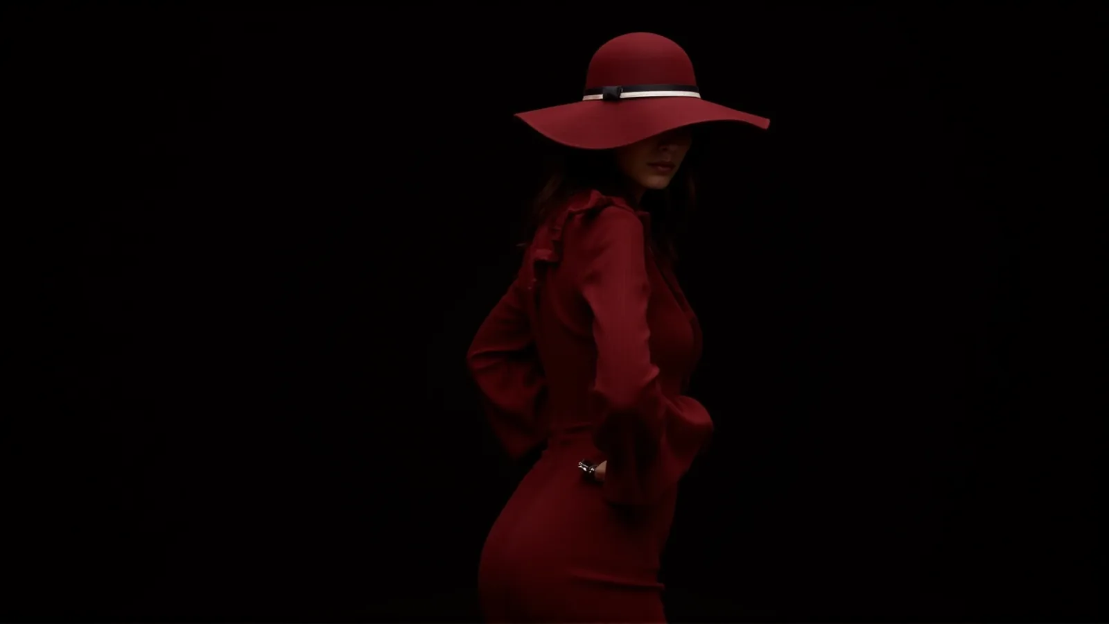 A woman in a red coat and wide-brimmed red hat, lit from the side against total darkness.